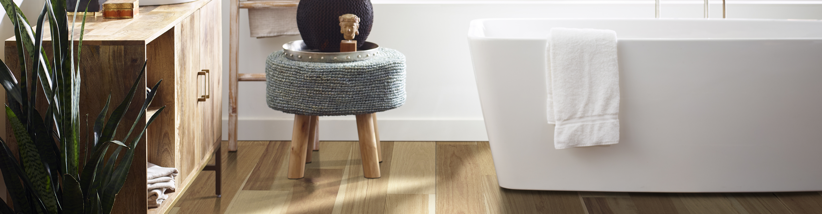 light wood flooring in white bathroom with white soaker tub and grey stool